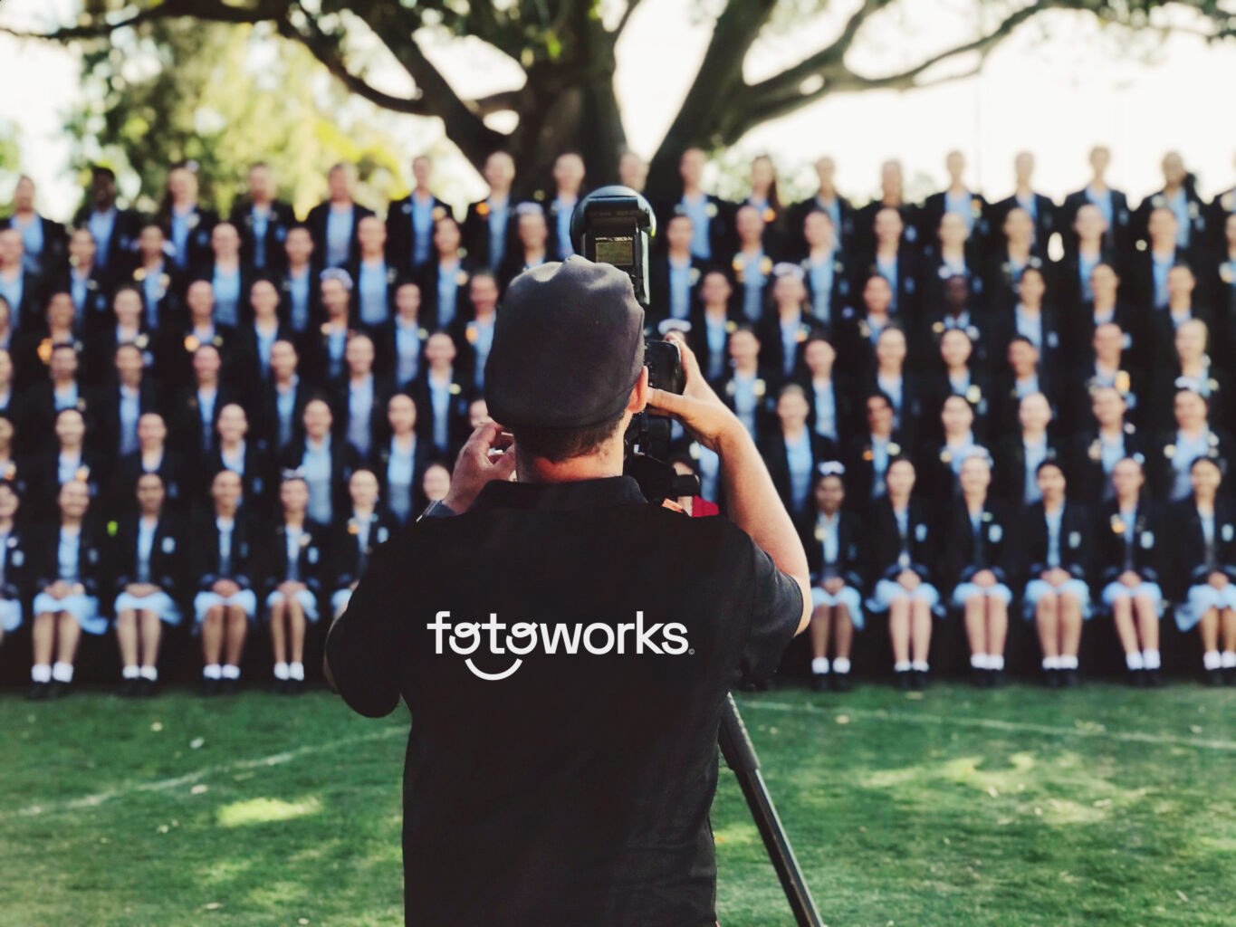 A Fotoworks team member taking a school class photo outside on the grass.